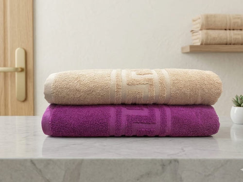 Two towels, one beige and one purple, stacked on a marble surface with a neutral background.